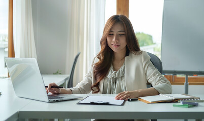 Attractive businesswoman using laptop computer and checking financial reports on white office desk.