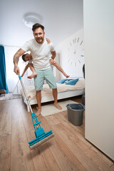 Boy clinging to man back while washing floor with mop