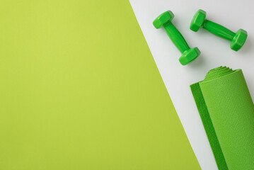 Fitness accessories concept. Top view photo of green sports mat and dumbbells on bicolor green and white background with copyspace