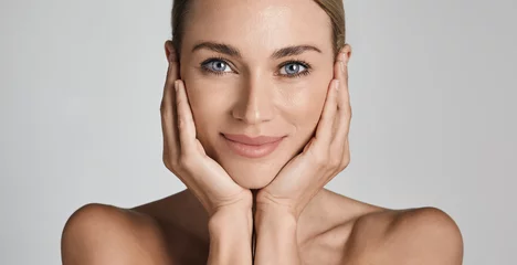Foto op Canvas Skin care. Beautiful woman with healthy facial skin touching hands moisturized face skin, on light grey background. High quality © Peakstock