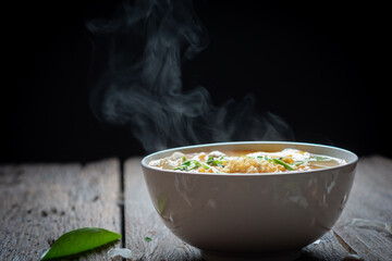 Noodles with steam and smoke in bowl on wooden background, selective focus. Asian meal on a table,...
