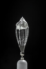 Metal whisk for whipping eggs with cream white raw meringue for perfect peaks isolated on black. Whipped cream, cookie recipe. vertical image. place for text