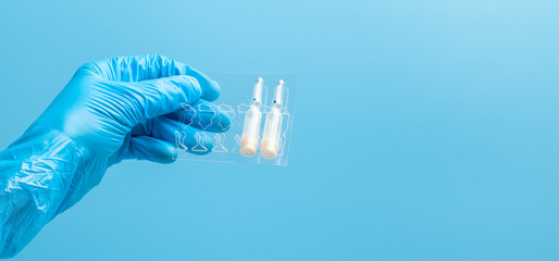 Medical glove. Ampoules with a white liquid in the hand in a blue medical glove. Isolated on a blue background.