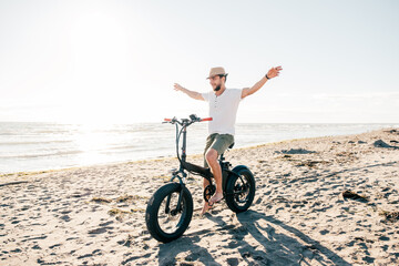 Fototapeta premium Young man on bicycle having fun with electric bike - carefree boy having fun and smiling on bicycle on the beach on a sunny day - freedom concept