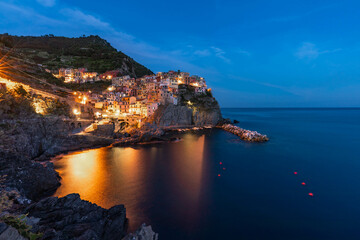 Fototapeta na wymiar Manarola at night. Illuminated Town at Mediterranean Sea in Italy. Famous Tourist destination in 5 Terre