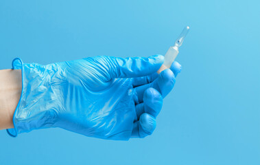 Medical glove. An ampoule with a white liquid in his hand in a blue medical glove. Isolated on a blue background.