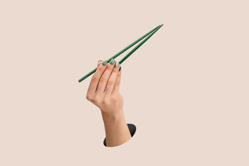 Female hand holding green chopsticks upright on clean pink background