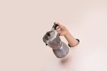 Female hand holding stovetop espresso coffee maker on clean pink background