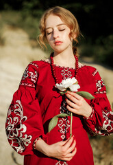 The girl in a traditional ethnic red dress posing outdoors with a white peony flower in her hand