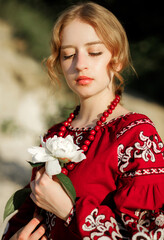 The girl in a traditional ethnic red dress posing outdoors with a white peony flower in her hand