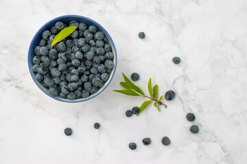 Blue honeysuckle sweet berries in a bowl on white marble table background. Top view, copy space, flat lay. Healthy eating concept. 