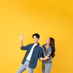 Two Young good looking asian couple using isolated on yellow background presenting to copy space feeling excited
