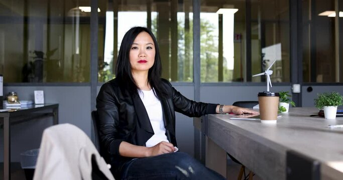 Cool businesswoman sitting at desk in office looking at camera