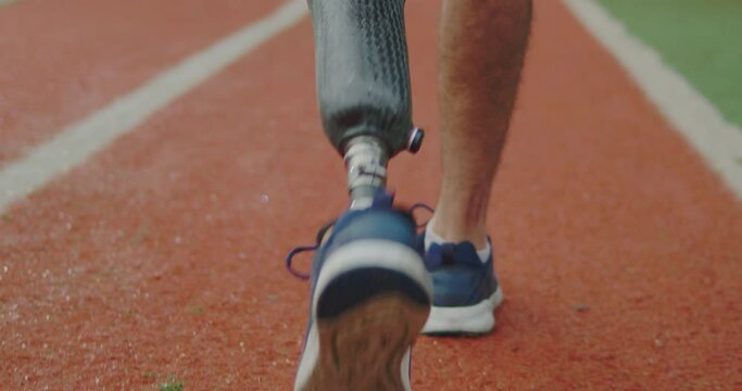 Man with prosthetic leg walking outside. Closeup of disabled Athlete. Amputee training on outdoor park stadium