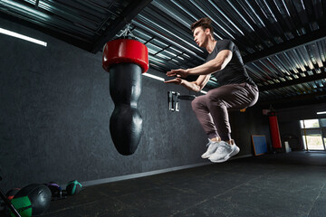 Sportsman doing tuck jumps in front of hanging punching bag