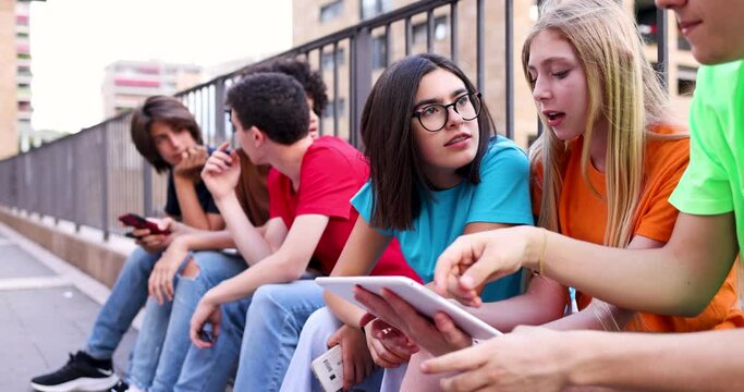 Group of teenagers using digital tablets sitting by railing