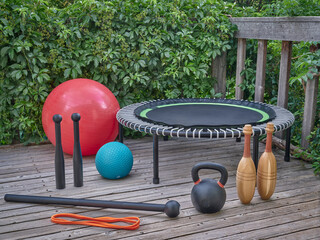 home gym concept - slam and Swiss balls, iron kettlebell, mini trampoline, resistance band, steel clubs, steel mace and wooden Indian clubs on a backyard patio