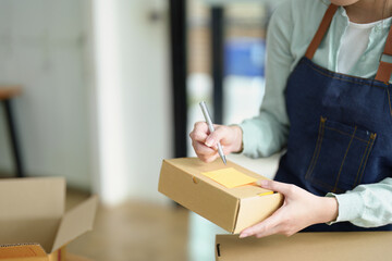 small startup, and SME owner, an Asian female entrepreneur, is writing down information on a notepad to organize the product before packing it into the inner box for the customer