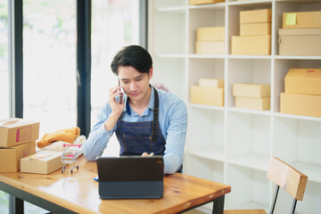 A portrait of a small start-up and SME owner, an Asian male entrepreneur using mobile phone, checking orders to organize products before packing them into inner boxes for customers