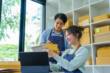Fototapeta na wymiar Portrait of a small start-up and SME owner, an Asian male and female entrepreneur checking orders and packing for customers, self-employed, freelance, online selling