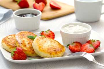 cottage sheese pancakes with fresh strawberries, mint leaves and sauce on a white dish. light background