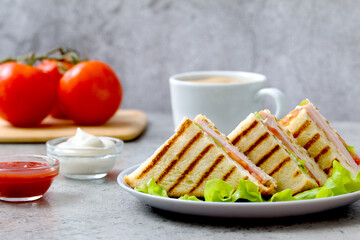 delicious grilled sandwiches with fresh lettuce on the background of tomatoes, sauces and a cup of coffee
