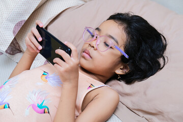 Asian kid looking to her mobile phone screen while laying in the bed