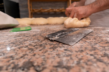 Close-up of a knife cutter for dough, in the background men's hands are kneading dough, there is a...