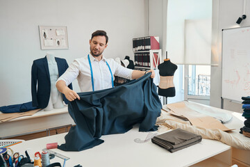 Man couturier is measuring big black fabric for tailoring