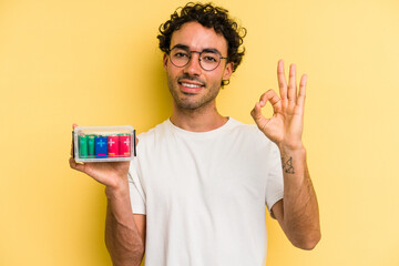 Young caucasian man holding a battery box isolated on yellow background cheerful and confident...