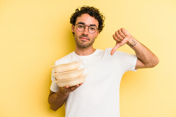 Young caucasian man holding tupper isolated on yellow background showing a dislike gesture, thumbs down. Disagreement concept.