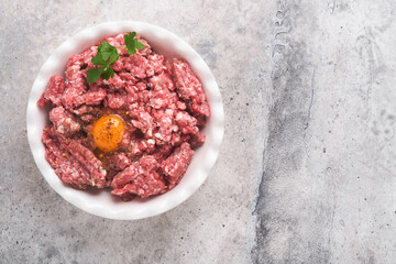 Raw minced meat. Ground meat beef, pork or lamb spices, herbs and eggs on white plate on light grey concrete background. Fresh minced meat ready for cooking. Food cooking background. Top view.