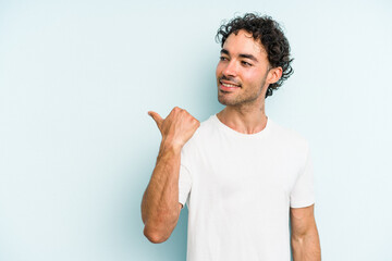 Young caucasian man isolated on blue background points with thumb finger away, laughing and carefree.