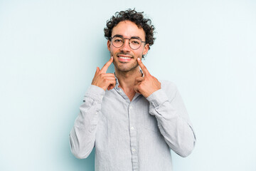 Young caucasian man isolated on blue background smiles, pointing fingers at mouth.