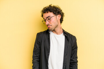 Young caucasian man isolated on yellow background shrugs shoulders and open eyes confused.