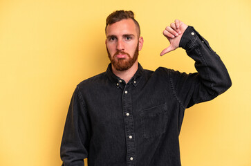 Young caucasian man isolated on yellow background showing a dislike gesture, thumbs down. Disagreement concept.