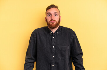 Fototapeta premium Young caucasian man isolated on yellow background shrugs shoulders and open eyes confused.