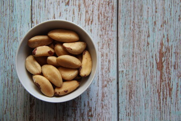 Brazil nuts or Amazon walnuts isolated in a white crockery bowl on a wooden table, top view. Bertholletia excelsa is a tree in the Lecythidaceae family.