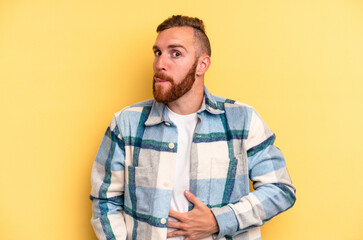 Young caucasian man isolated on yellow background touches tummy, smiles gently, eating and satisfaction concept.