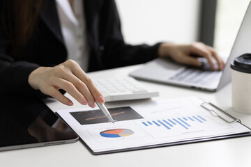 Businesswoman holding pen pointing at company sales report financial documents to analyze financial planning and growth marketing.