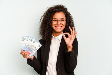 Young business Brazilian woman holding banknotes isolated on white background cheerful and confident showing ok gesture.