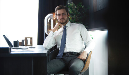 Portrait of businessman sitting in office, successful man worker employee by work desk looking at camera
