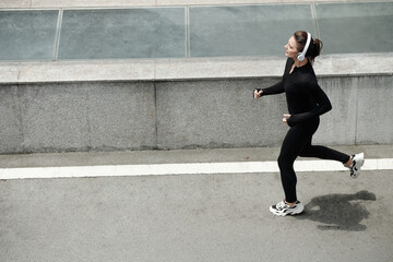 Young female athlete listening to music in headphones while running in the morning outdoors