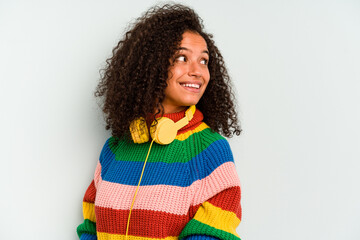 Young Brazilian woman listening to music isolated on blue background looks aside smiling, cheerful...
