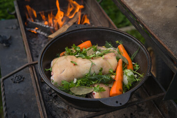 the process of cooking a dish on a fire in a cauldron. pork knuckle in beer with vegetables. the...
