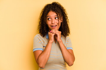 Young Brazilian woman isolated on yellow background praying for luck, amazed and opening mouth looking to front.