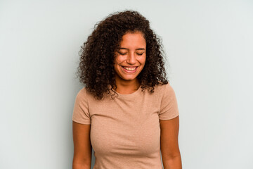 Young Brazilian woman isolated on blue background laughs and closes eyes, feels relaxed and happy.
