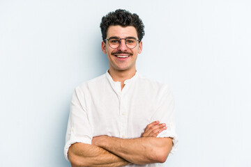 Young caucasian man isolated on blue background who feels confident, crossing arms with determination.