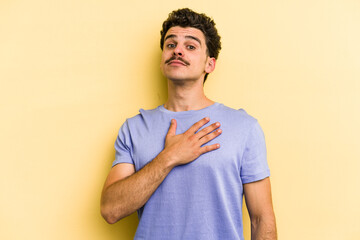 Young caucasian man isolated on yellow background taking an oath, putting hand on chest.