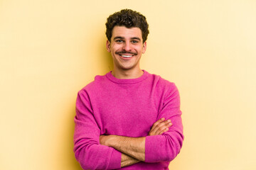 Young caucasian man isolated on yellow background who feels confident, crossing arms with determination.